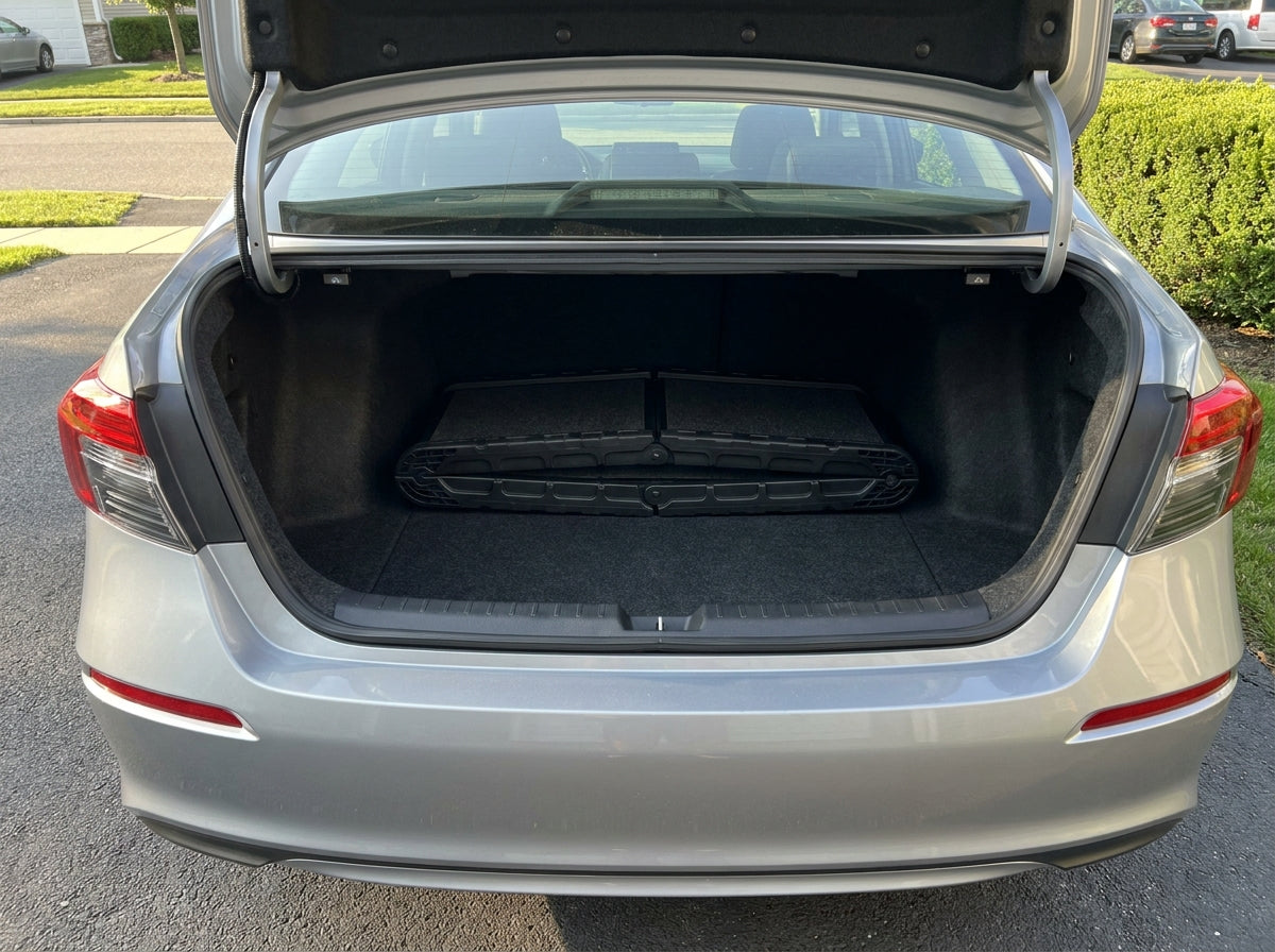 A folded black bi-fold dog car ramp lying flat on the carpeted floor of a sedan trunk.