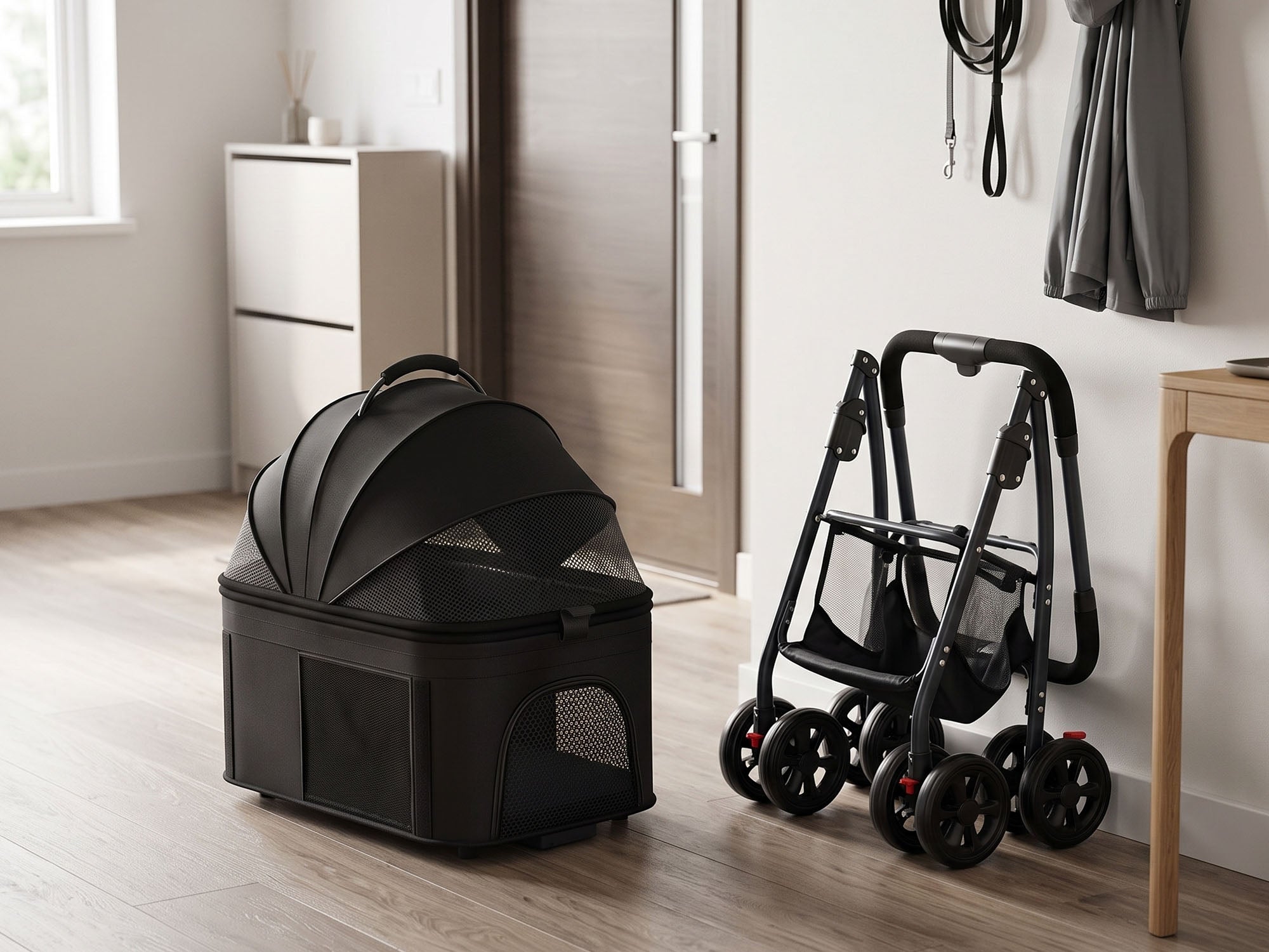 A black pet carrier with a handle and mesh windows sits on a light wood floor next to its compactly folded stroller frame, leaning against a neutral-colored wall in a home entryway. Coats and leashes hang in the background.